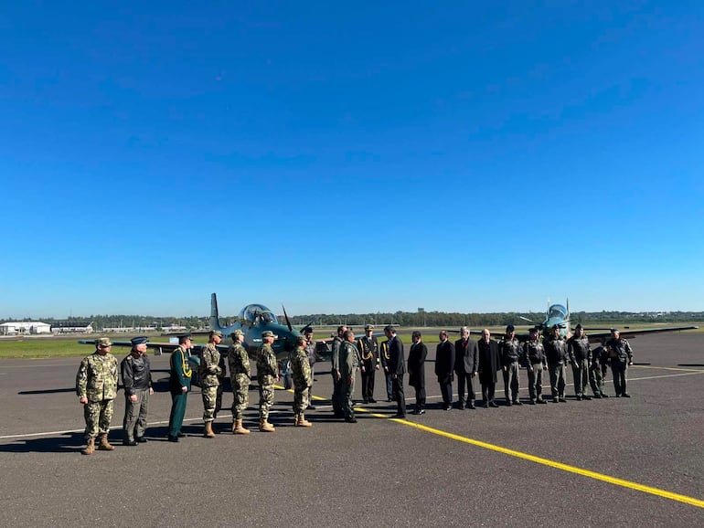 Formación de soldados y funcionarios en uniforme militar y trajes formales, bajo un cielo soleado, en ceremonia oficial.