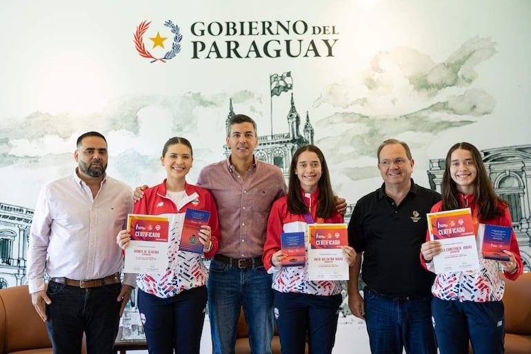 Santiago Peña y César Ramírez sonríen durante la entrega de certificados a los integrantes del Team Paraguay, con chaquetas deportivas rojas y blancas.