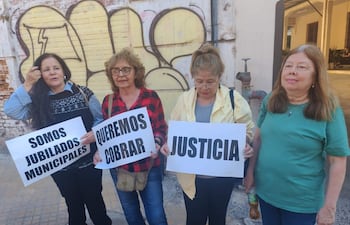 Cuatro mujeres jubiladas con pancartas en una manifestación, vestidas con ropa de colores variados, expresiones serias y activas en un entorno urbano.