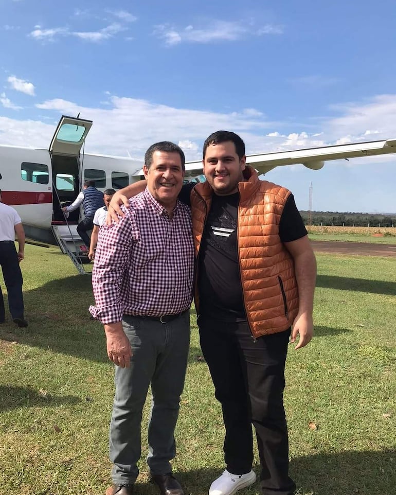 Horacio Cartes sonríe junto a José Emilio Vázquez Acosta, ambos en un aeródromo, rodeados por un ambiente amigable.