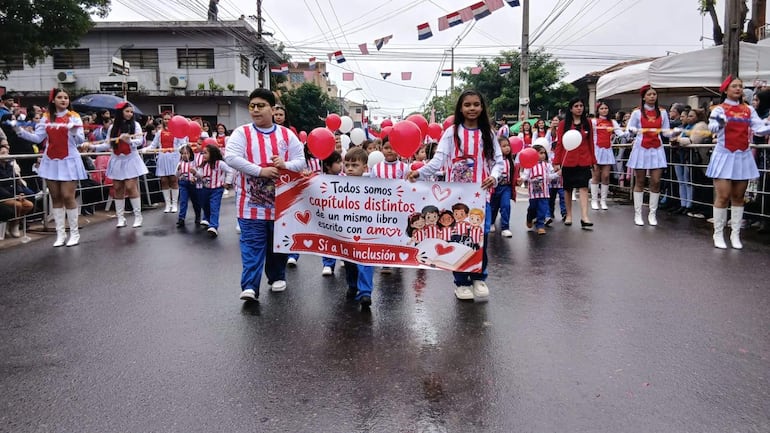Grupo de niños y jóvenes con camisetas rojas y blancas del Club Olimpia, sosteniendo globos y un cartel sobre inclusión.