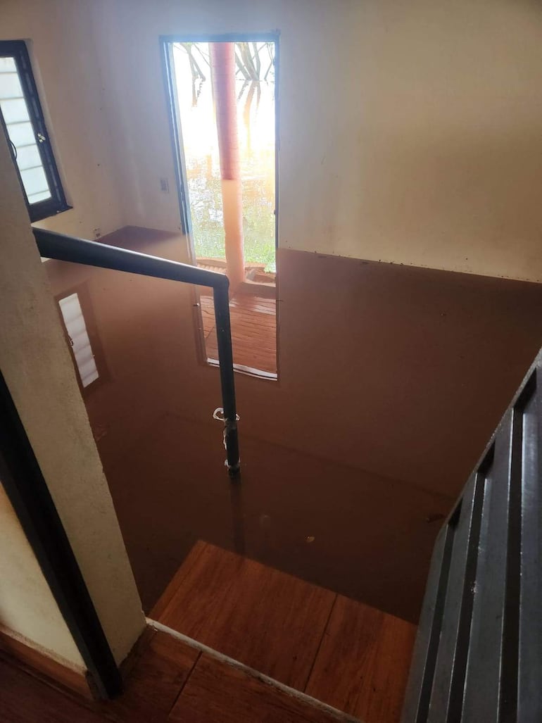 Interior de una oficina inundada con agua marrón y un pasamanos negro visible.