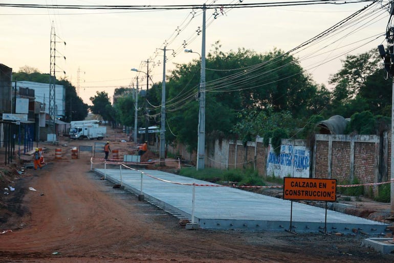 Calle en construcción con calzada de concreto y cartel naranja de 'calzada en construcción', postes de luz visibles.