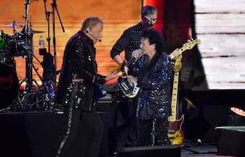 Músicos de Air Supply en el escenario, vestidos con trajes brillantes, interactuando bajo luces coloridas durante un concierto.