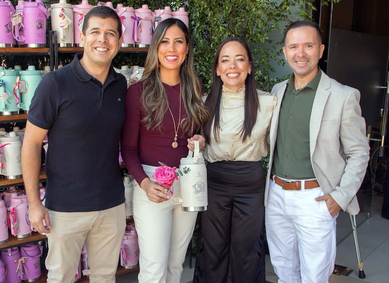 Dos hombres y dos mujeres sonríen en evento del Día de la Madre, rodeados de decoración colorida y recipientes en la estantería.