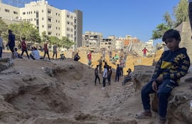 En una fosa común improvisada detrás del Hospital Shifa, en la ciudad de Gaza, decenas de familias entierran a sus seres queridos este domingo, mientras la operación terrestre de Israel se expande, temerosos de que buscar un lugar de entierro digno les ponga en riesgo. Los cuerpos, envueltos en telas blancas, son depositados en un hoyo abierto en la arena. A su alrededor, edificios derrumbados y el zumbido constante de drones conforman el escenario de un duelo sin pausa. EFE/ Ahmad Awad