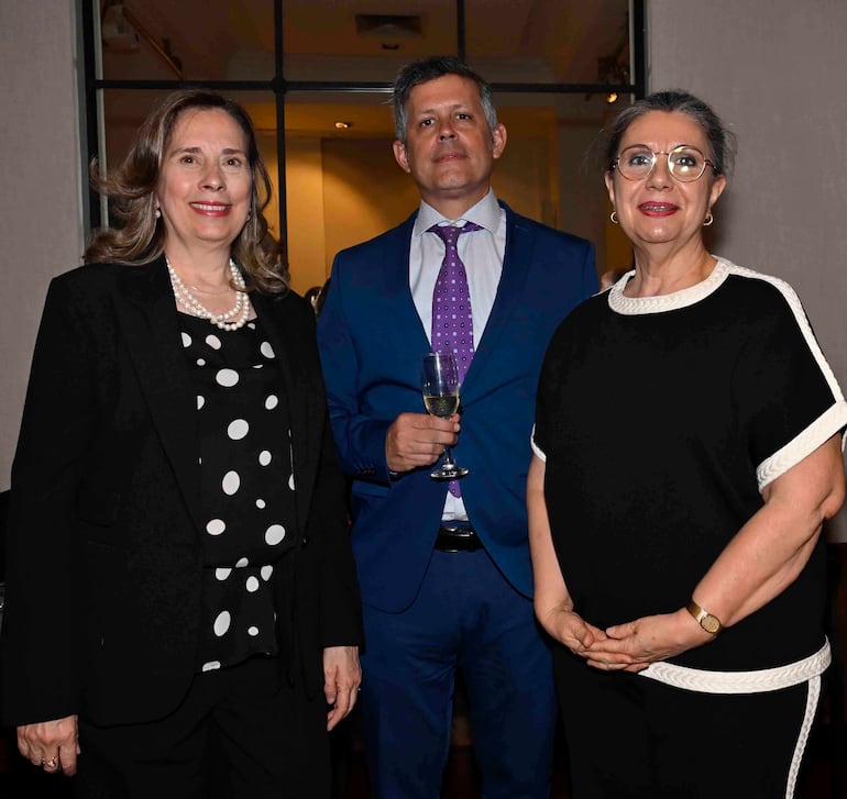 Diana Díaz de Espada con blusa negra, Teresa Rojas con gafas y blusa negra conversan en un ambiente elegante mientras un hombre sostiene una copa.