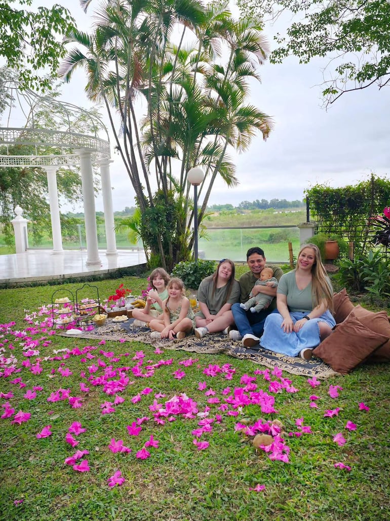 Cinco personas, incluidos cuatro niños, en vestimenta casual, sentados en césped decorado con flores rosadas, aparentando felicidad.