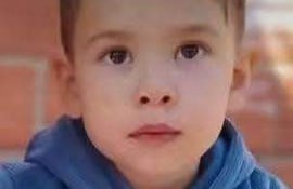 Khael Valdez, niño de 3 años, sentado con hoodie azul y pantalones naranjas, sostiene un vaso blanco en un entorno tranquilo.
