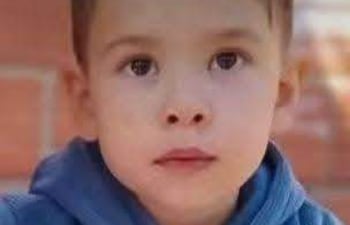 Khael Valdez, niño de 3 años, sentado con hoodie azul y pantalones naranjas, sostiene un vaso blanco en un entorno tranquilo.
