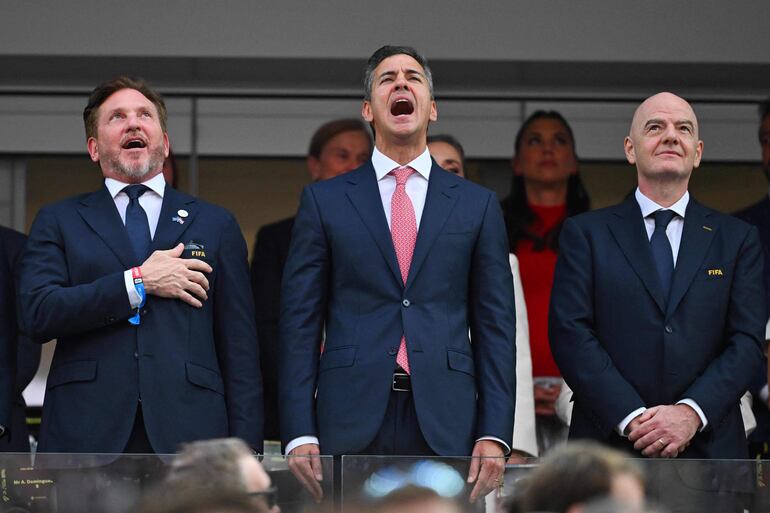 El presidente de la CONMEBOL, Alejandro Domínguez, y el presidente de Paraguay, Santiago Peña, cantan el himno nacional paraguayo junto al presidente de la FIFA, Gianni Infantino, antes del partido de fútbol del Grupo D de la Copa Mundial 2026 entre Estados Unidos y Paraguay.