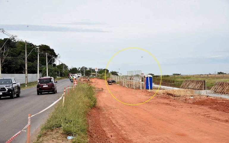 Escena de construcción con camino de tierra, vehículos en movimiento y valla de seguridad. Sin personas visibles.