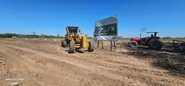 Máquina amarilla y tractor rojo en campo agrícola con cartel de construcción del complejo municipal.