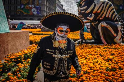 "Un hombre disfrazado pasa junto a flores de cempasúchil (caléndulas) durante las celebraciones anuales del Día de Muertos en la Ciudad de México el 2 de noviembre de 2025.