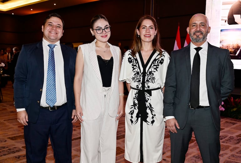 Cuatro personas sonrientes: hombre de boleto azul, mujer con traje a rayas, mujer en vestido floral y hombre con barba en traje gris.