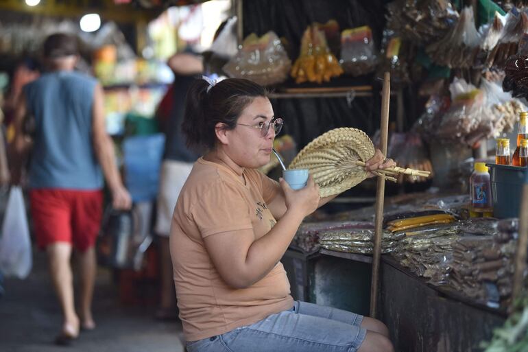 Una mujer se abanica y toma tereré para aplacar el calor. 
