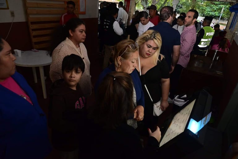 Cuatro mujeres y un niño en un centro de votación; mujeres serias observan pantalla mientras el niño muestra curiosidad.