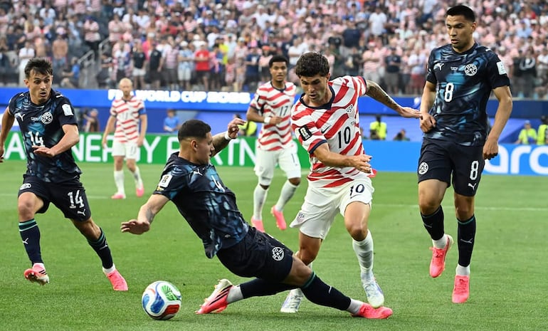 Jugadores de Paraguay y Estados Unidos luchan por el balón en el estadio SoFi, con hinchas al fondo en un ambiente competitivo.