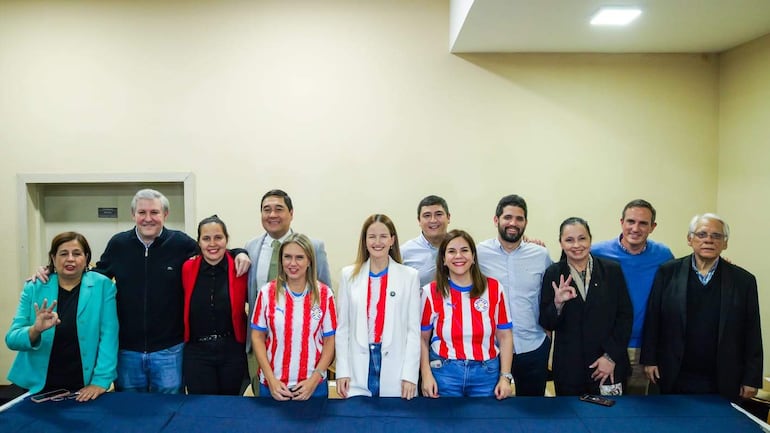 Soledad Núñez sonriente en el centro, rodeada de simpatizantes, algunos llevan camisetas del equipo nacional de fútbol y expresan alegría.