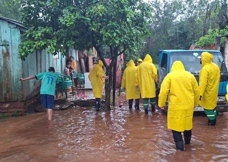 Grupo de personas con impermeables amarillos caminan hacia una camioneta, rodeados de agua, con un niño con camiseta de Neymar Jr.