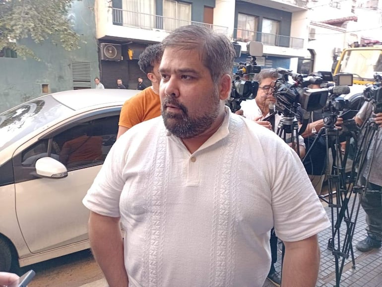 Ivo Brun, hombre robusto con barba y camiseta blanca, atendiendo a la prensa rodeado de cámaras en un entorno urbano.