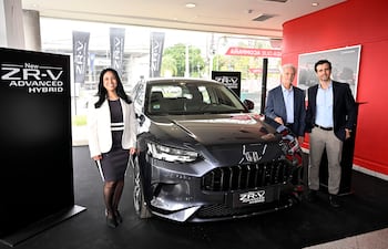 Mujer sonriente con traje blanco y negro junto al vehículo gris Honda ZR-V, acompañada de dos hombres en un ambiente moderno y profesional.