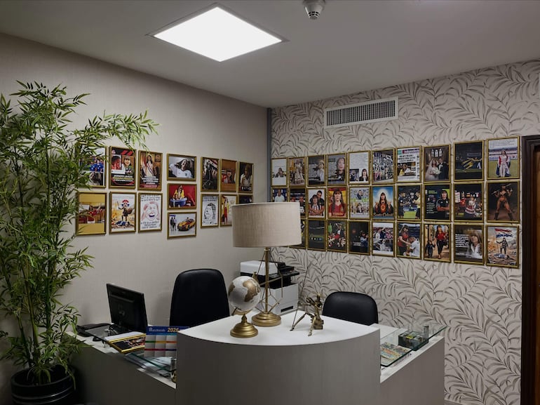 Despacho vacío con decoración moderna, fotos enmarcadas en la pared, planta a la izquierda y una mesa con objetos decorativos.