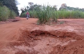 Ciclista con ropa oscura pedalea por un camino de tierra rodeado de vegetación, con un bache visible a la izquierda.