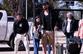 Omar Alderete con gorra y maleta, rodeado de personas sonrientes en un ambiente natural.