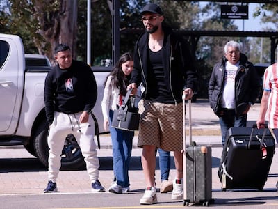 Omar Alderete con gorra y maleta, rodeado de personas sonrientes en un ambiente natural.