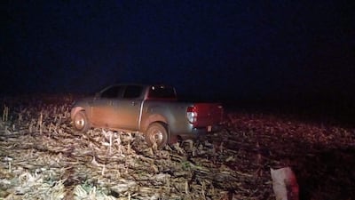 Camioneta gris cubierta de tierra, estacionada en un campo agrícola con restos de maíz, en ambiente nocturno.