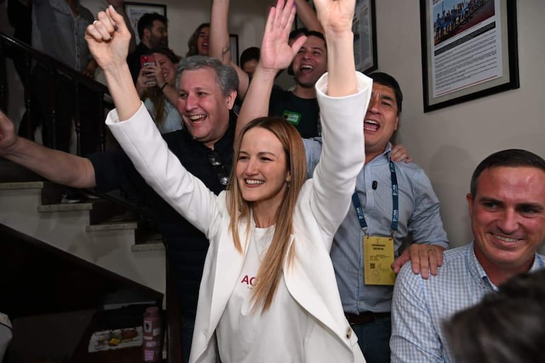 Soledad Núñez con blazer blanco y sonrisa amplia, rodeada de personas alegres, incluido Rafael Filizzola, en un ambiente festivo.