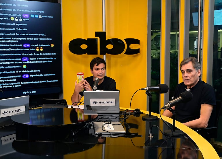 Víctor Pecci, mayor, con expresión neutral, escucha a un hombre joven en camiseta negra hablando al micrófono en un estudio con logotipo de ABC Color.