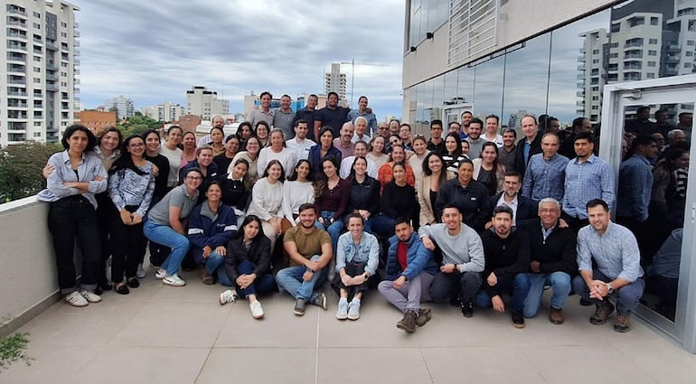 Grupo de 70 personas sonriendo y posando juntas en un espacio exterior, vistiendo ropa casual en un ambiente urbano.