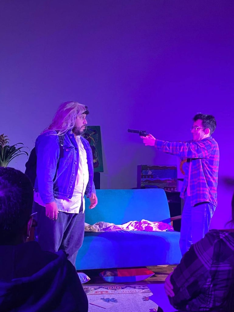 Personajes en el ICPA; uno con peluca rubia y chaqueta de mezclilla, otro sosteniendo pistola en ambiente dramático y luces púrpuras.