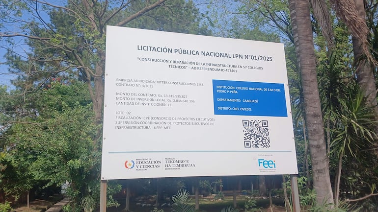 Cartel de licitación pública con información sobre la construcción en el entorno de árboles y vegetación.