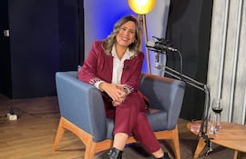 Katy González sonriente en sillón azul con traje burdeos y blusa blanca, rodeada de un ambiente acogedor en un estudio.