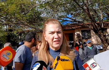 María Teresa Barán, con blusa azul oscuro y cabello rubio, habla a la prensa, rodeada de personas con micrófonos en un entorno natural.