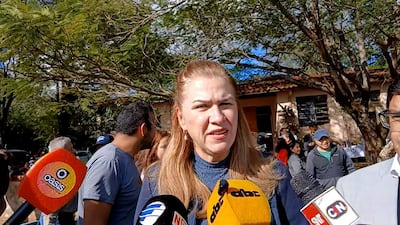 María Teresa Barán, con blusa azul oscuro y cabello rubio, habla a la prensa, rodeada de personas con micrófonos en un entorno natural.