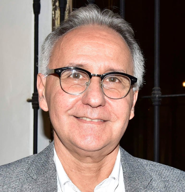 Hombre con gafas y sonrisa, posando en un retrato en ambiente formal, vestido adecuadamente.