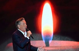 Ricardo Montaner canta con micrófono en mano, vistiendo traje oscuro y camisa blanca, bajo una iluminación cálida en el escenario.