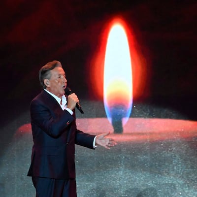 Ricardo Montaner canta con micrófono en mano, vistiendo traje oscuro y camisa blanca, bajo una iluminación cálida en el escenario.