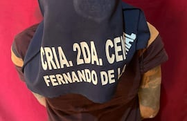 Hombre de espaldas con camiseta oscura y cabeza cubierta, en un entorno de color rojo, probablemente durante su detención.