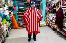 Hombre sonriente con poncho rojo y blanco en tienda repleta de mantas coloridas durante el festival.