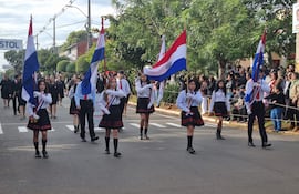 Grupo de jóvenes en camisas blancas y faldas negras con banderas, simbolizando la celebración patriótica en un ambiente festivo.