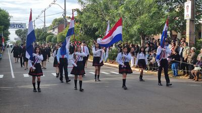 Grupo de jóvenes en camisas blancas y faldas negras con banderas, simbolizando la celebración patriótica en un ambiente festivo.