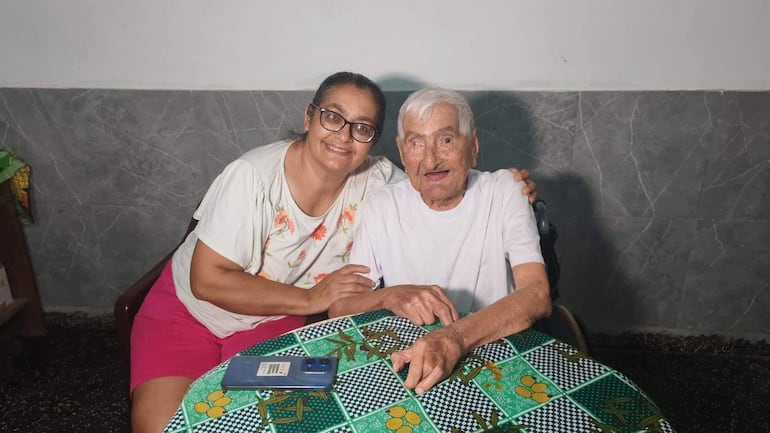 Canuto González con camiseta blanca, sonríe abrazando a una mujer con gafas, camiseta blanca con flores y pantalones cortos rosas.