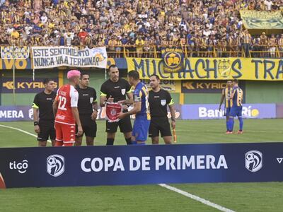 Guillermo Hauché (i), jugador de General Caballero de Juan León Mallorquín, y Pablo Aguilar (d), futbolista de Sportivo Luqueño, con el árbitro en el sorteo de un partido por el torneo Apertura 2023 del fútbol paraguayo en el Feliciano Cáceres, en Luque.
