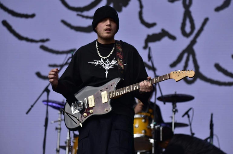 Músico de Dentro del Sol tocando guitarra eléctrica, con gorro negro y camiseta negra, en escena vibrante del festival.