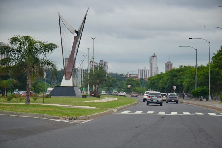 Escultura en forma de arpa en la avenida, rodeada de tráfico y edificios en un día nublado.